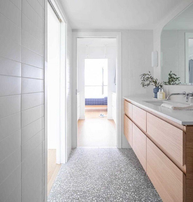 Gạch terrazzo từ bếp tiếp tục xuất hiện trong phòng tắm, kết hợp với tủ gỗ tự nhiên, mang lại sự liền mạch trong thiết kế và cảm giác ấm áp. 